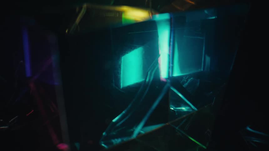 A rotating glass prism reflects colorful light beams against a dark background