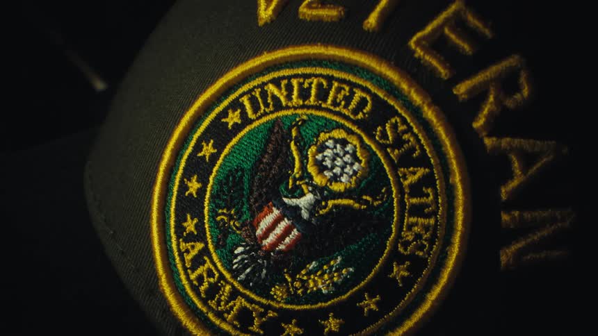 A close view of an embroidered united states army patch on a black hat with the word veteran stitched in yellow thread above the circular emblem