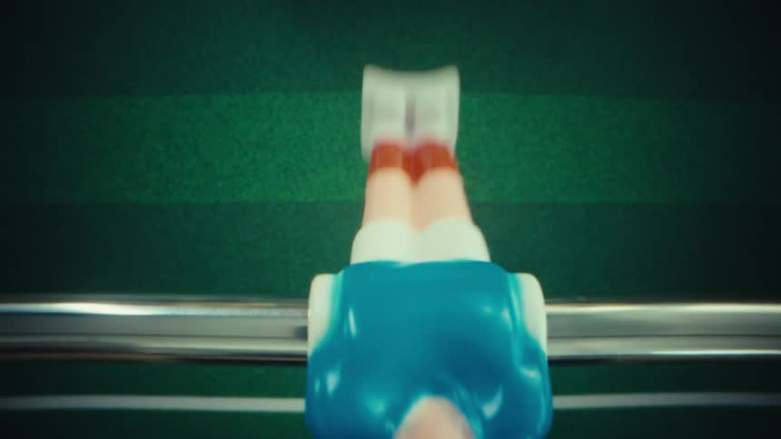 A view from above shows a blue plastic figure on a metal rod hitting a small soccer ball across a green table while playing a game of table football