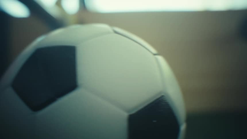 A soccer ball rolls into the frame inside a foosball toy with wooden players and a blurry background