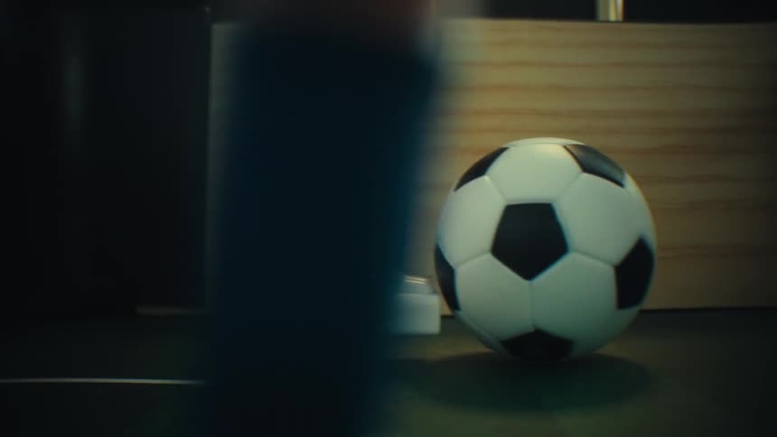 A close view moves past a plastic figure to show a small soccer ball on a green table before being kicked of another player while playing table football