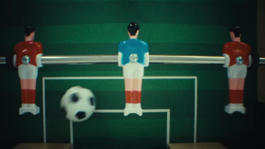 A foosball table is shown from an overhead perspective as the game pieces move across the field