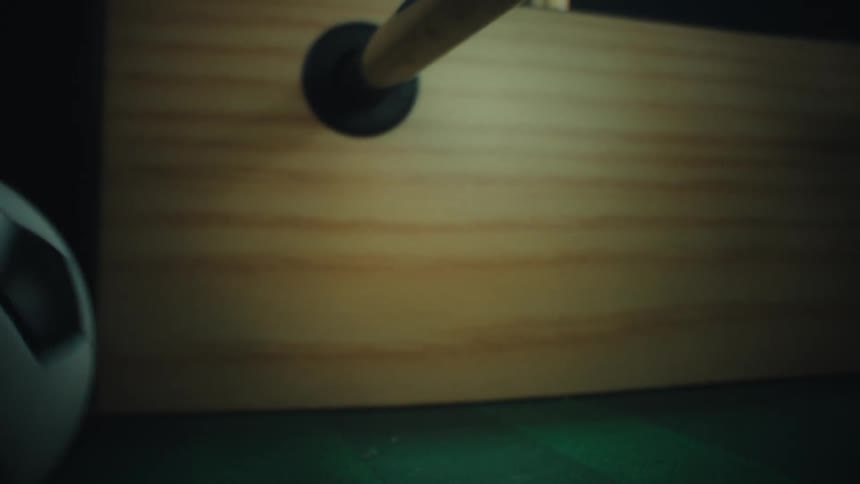 Foosball player figure attached to a metal rod kicking a ball on a game table