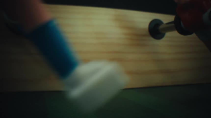 Blurred soccer ball in the foreground on a foosball table with a player figure and metal rod