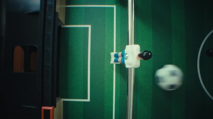 Foosball player figures attached to metal rods over a green field with a moving ball