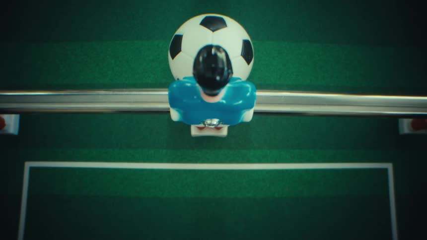 A close view shows a black and white soccer ball and the plastic players on a table soccer game