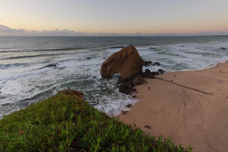 Large isolated rock surrounded by ocean waves on a sandy beach
