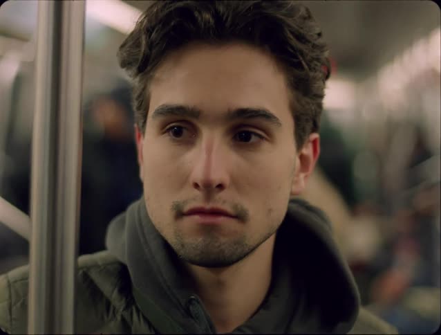 Young adult man standing on a train surrounded by other people indoors