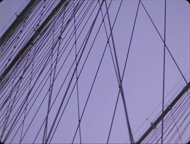 A view from below shows the massive stone arch and many steel cables of a large bridge against a purple twilight sky