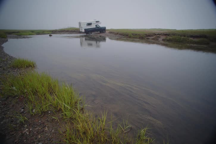 Truck with a camper on back crosses a shallow stream of water