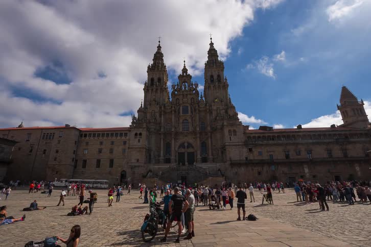 A group of tourists walking outside the cathedral of santiago de compostela on a sunny day