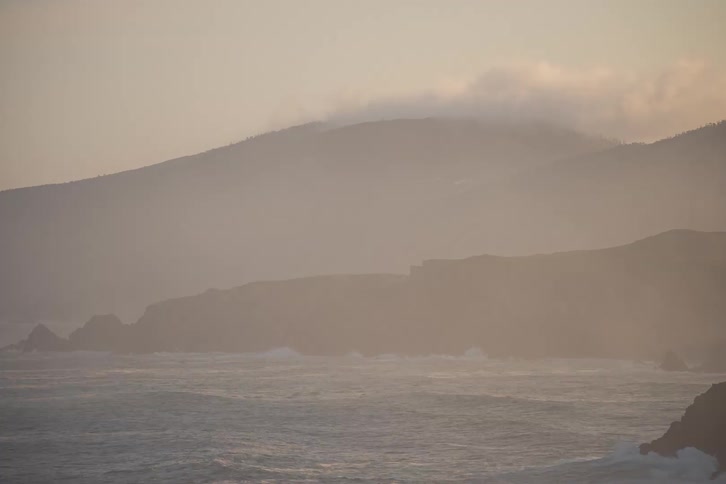 Clouds move over mountains as river water flows along the coast
