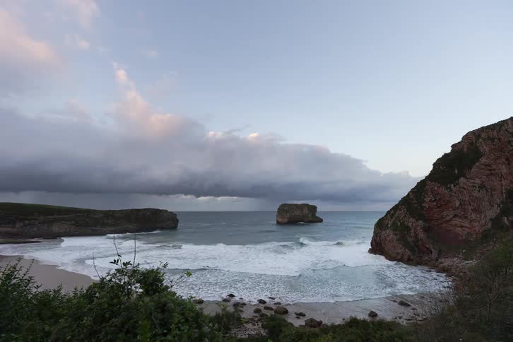 Ocean waves moving toward a beach between cliffs with a rocky island at the center