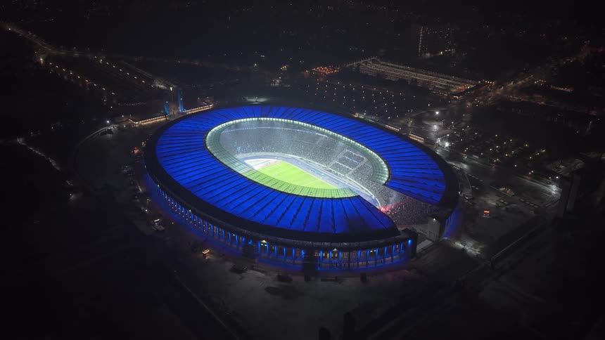 Stadium illuminated in blue seen from above at night in an urban area