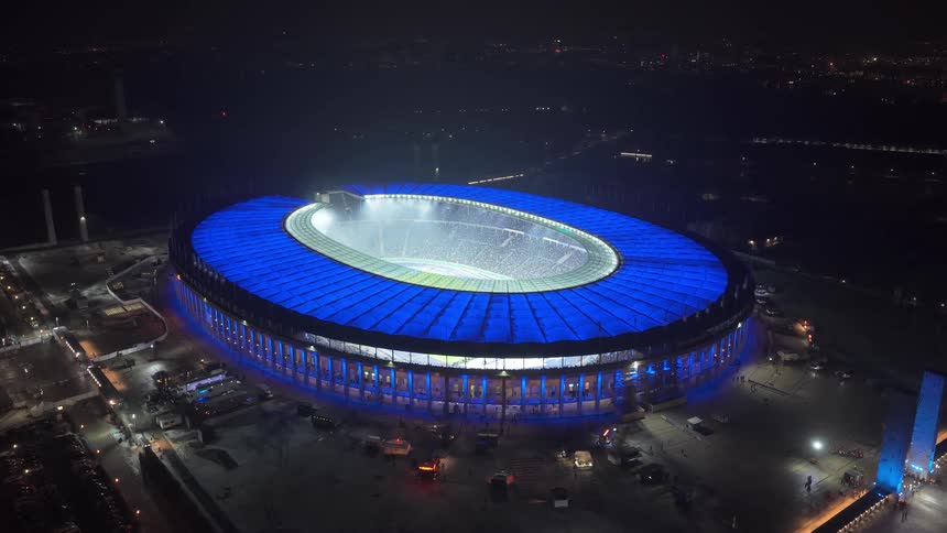 Stadium illuminated at night seen from an aerial perspective with a soccer field in the center