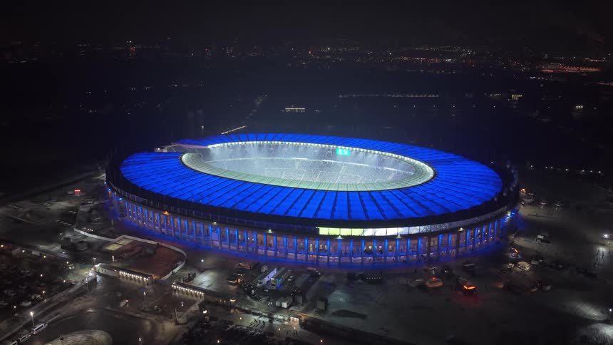 Oval stadium illuminated at night seen from above with a soccer field in the center