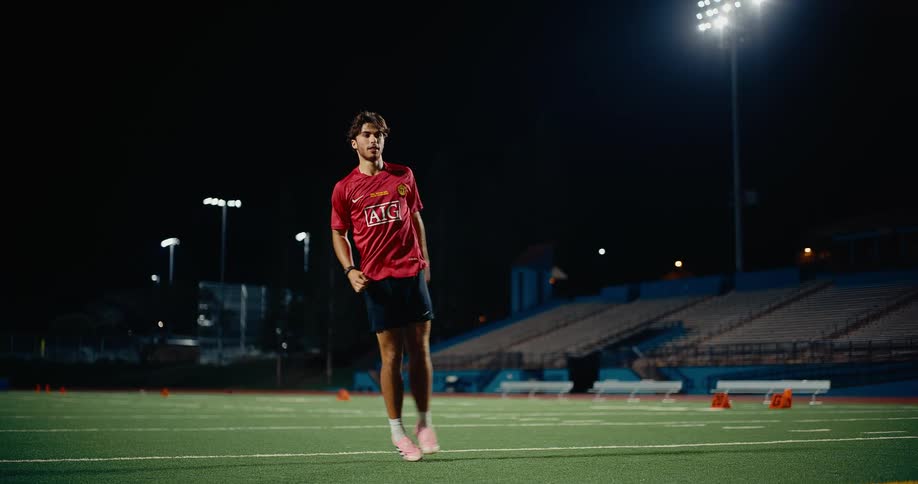 A male soccer player kicks a ball on an outdoor field at night