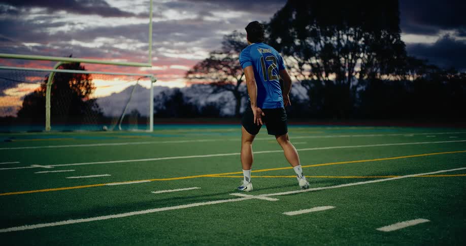 Player wearing number 12 jersey kicking a ball on a sports field at sunset