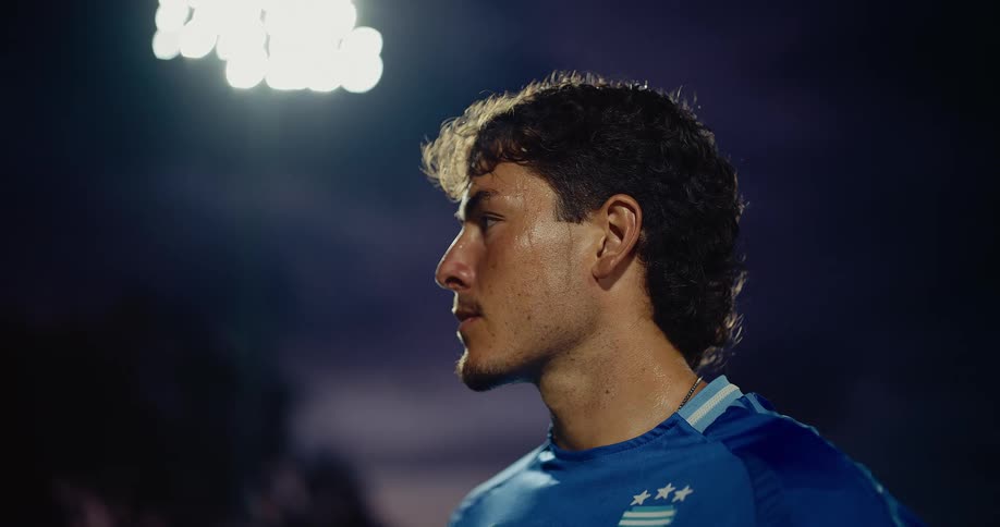 Soccer player wearing a blue jersey looking to the side on a field illuminated at night