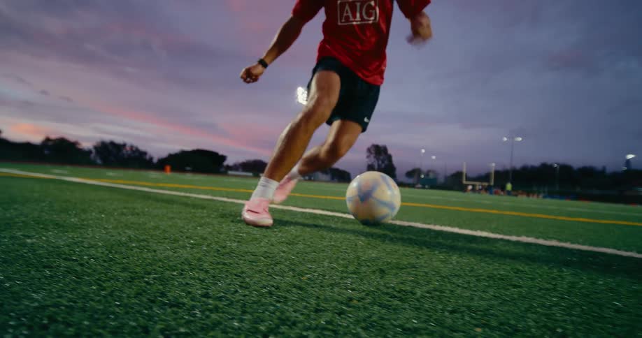 Soccer player kicks the ball moving it down the field and outside of the white line
