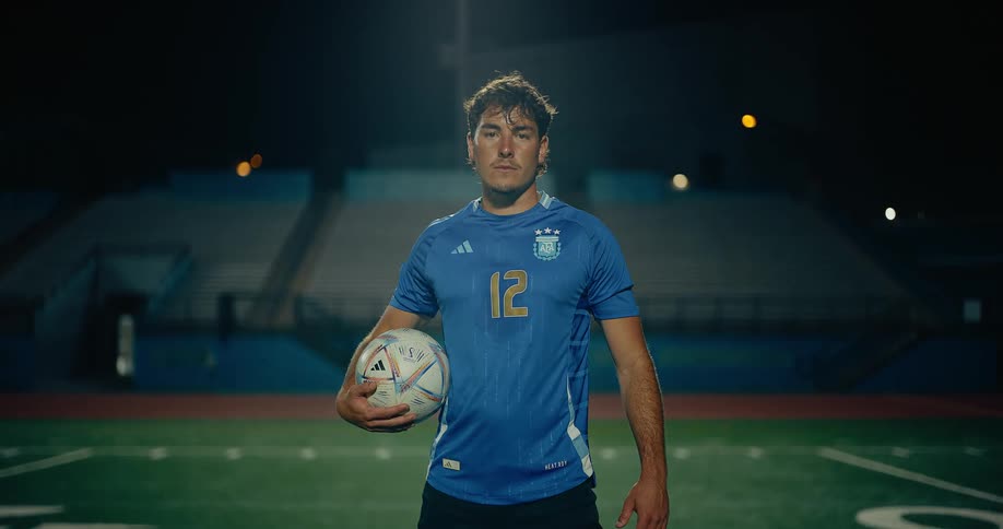 A soccer player standing on the grassfield holding a ball at night