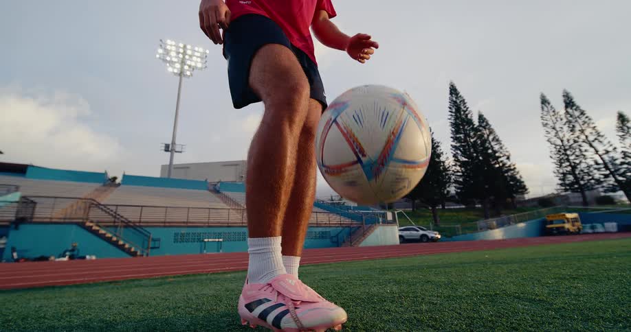 Soccer player standing in a field bouncing a soccer ball into the air with his feet
