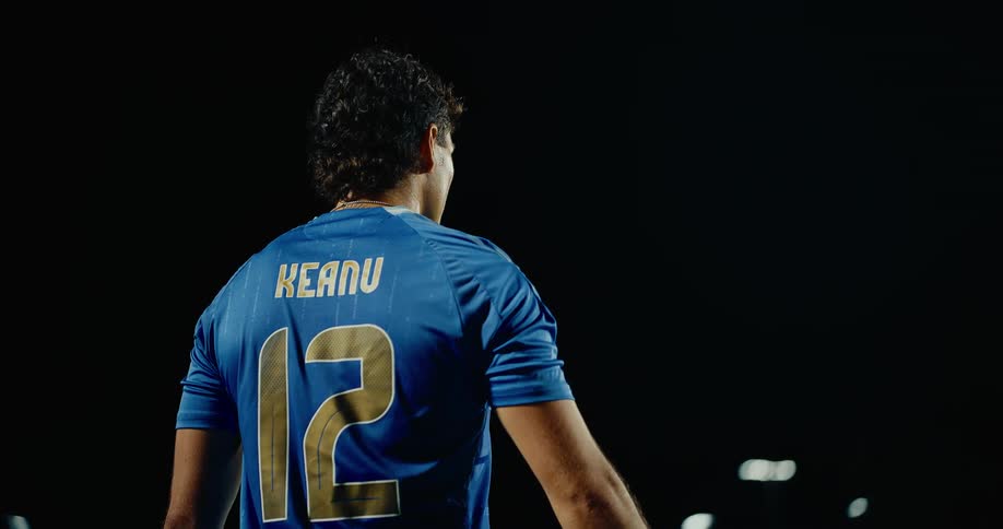 Player wearing blue number 12 jersey holding a ball on a field illuminated at night