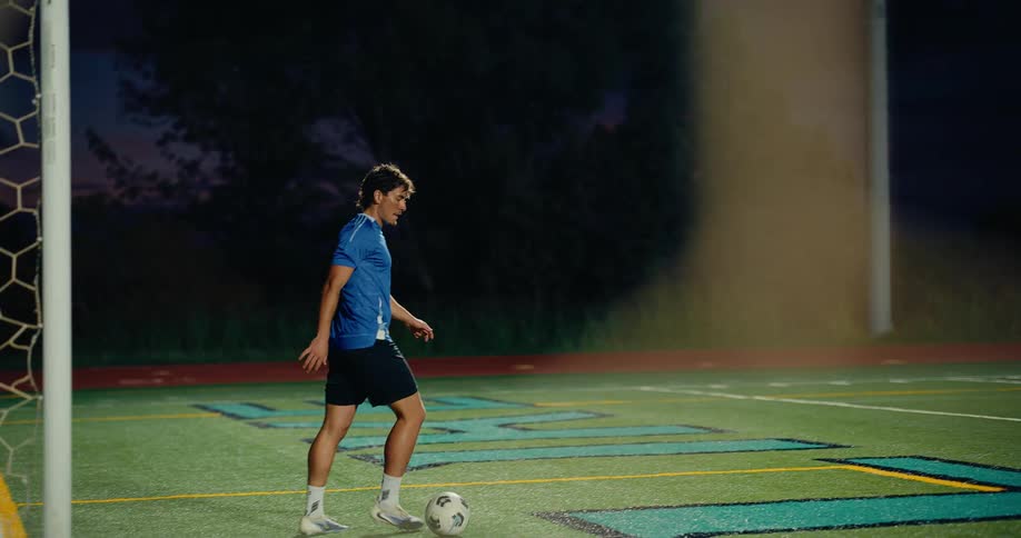 Male athlete moves a soccer ball on a soccer field at night