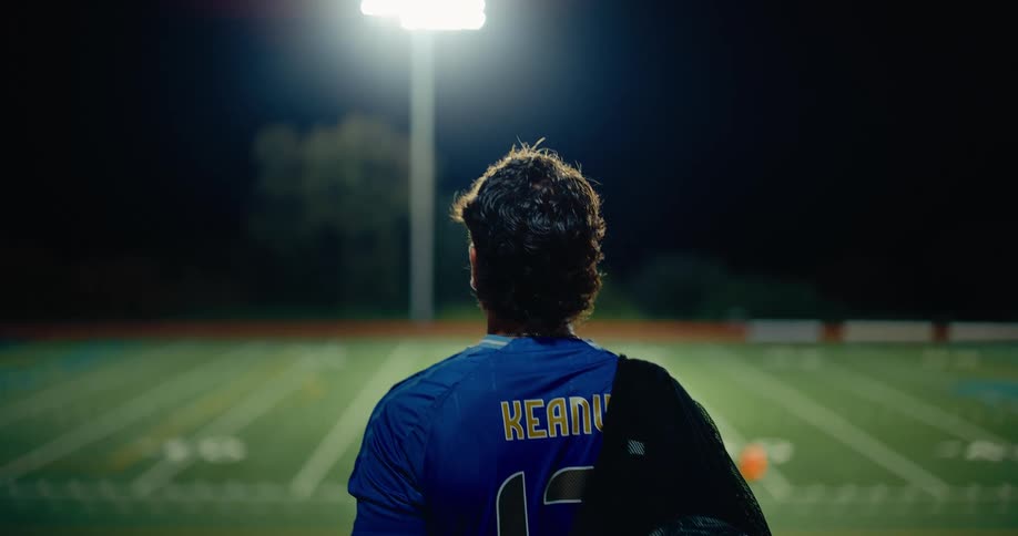 Player wearing blue number 12 jersey walking on a sports field illuminated at night