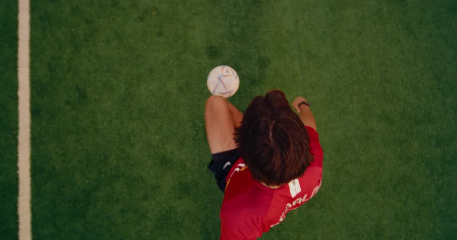 A man wearing a red ronaldo jersey juggles a soccer ball on a green turf field
