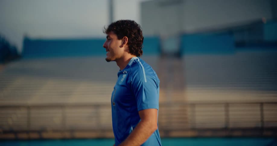 Young adult man wearing a soccer uniform kicking a ball on a sports stadium outdoors during dusk or dawn