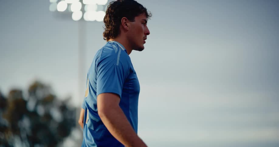 A soccer player in a blue jersey with the number 12 practices juggling and kicking a ball on a fieldthe scene is captured at dusk under bright stadium lights featuring closeup shots of the athletes focused movements