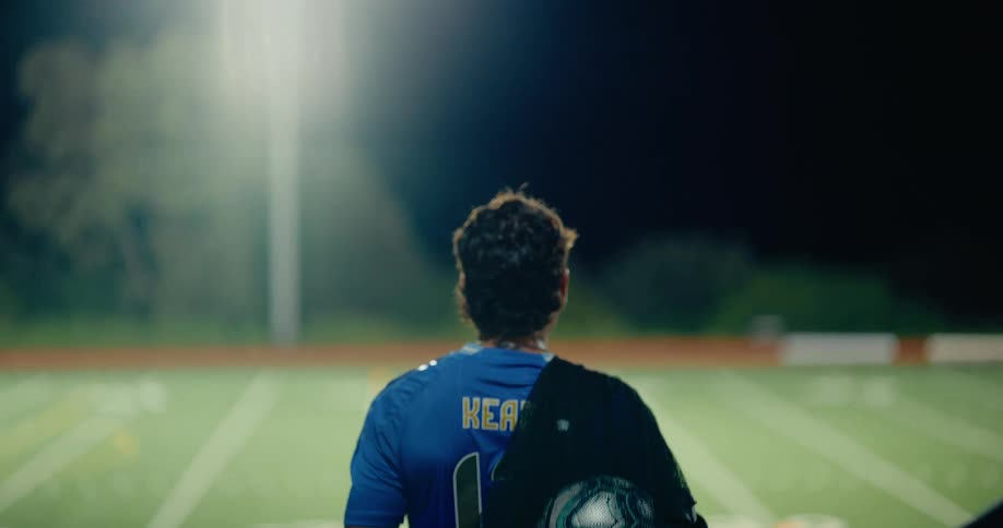 Young man walks down stairs to a playing field with a bag of soccer balls over his shoulder