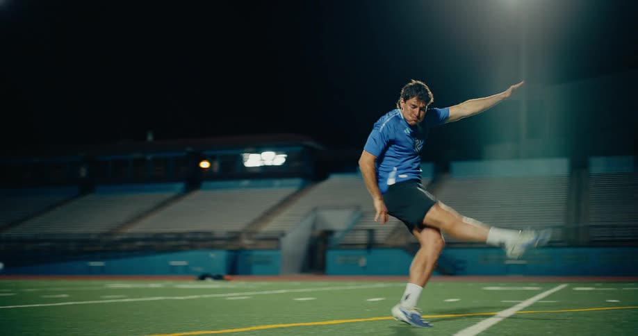 A soccer player kicking a soccer ball across a football training pitch at night