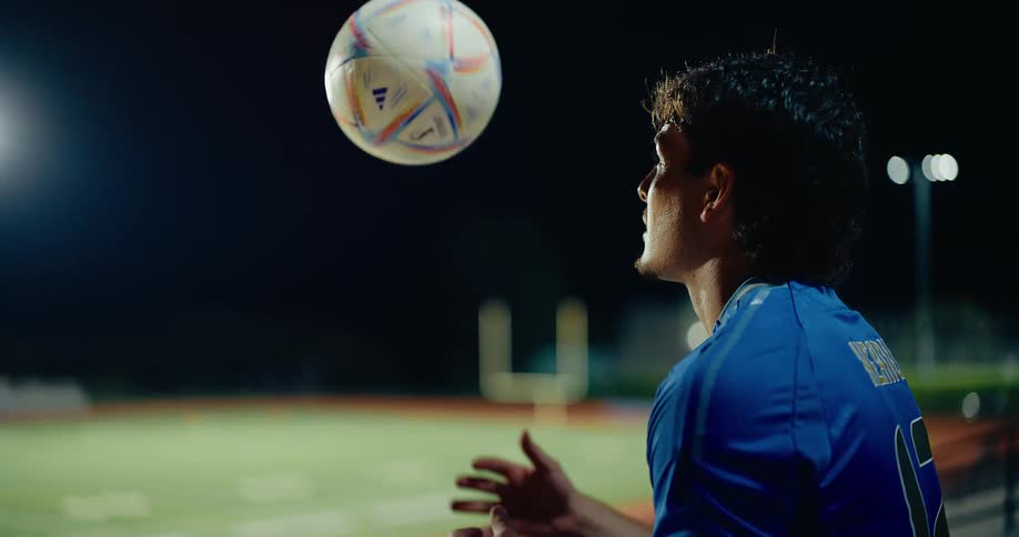 A soccer player stands in the bleachers and tosses a soccer ball at night