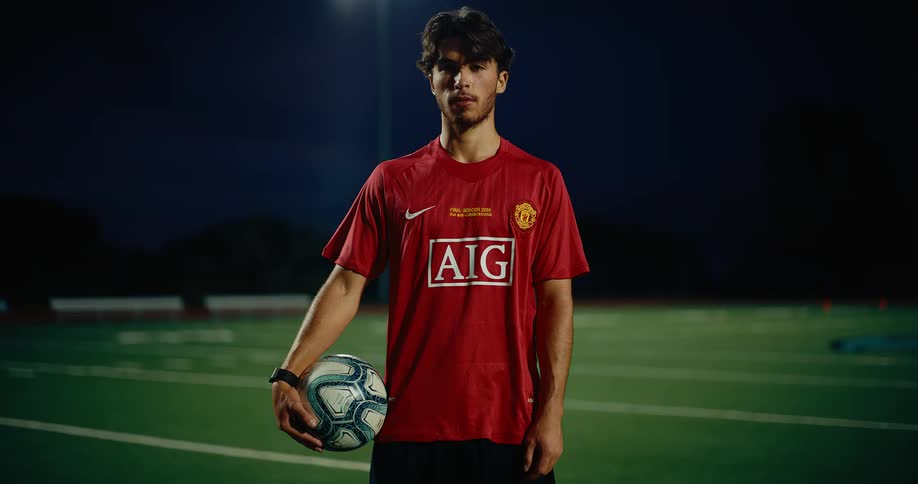 Player wearing a red jersey holding a soccer ball on a sports field at night
