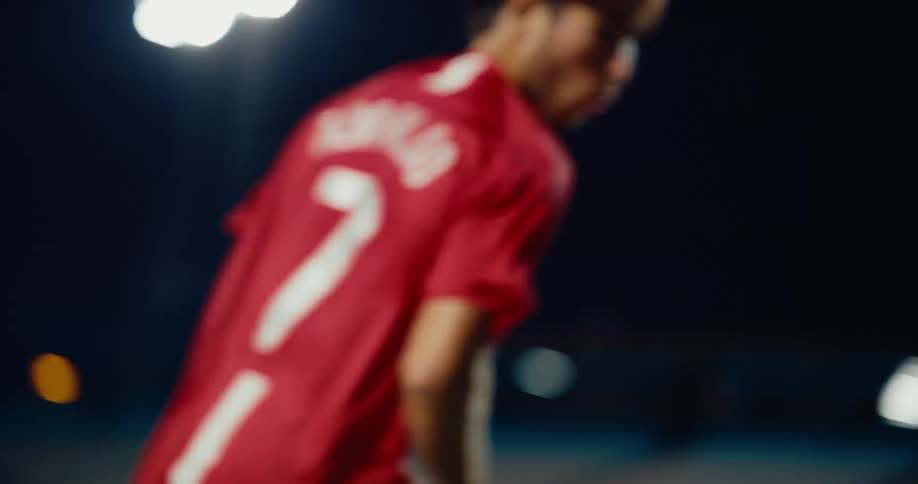A soccer players powerful leg kicks a soccer ball through the night air on a lit field sending a pinkcleated foot forward in a dynamic moment of motion and athletic focus