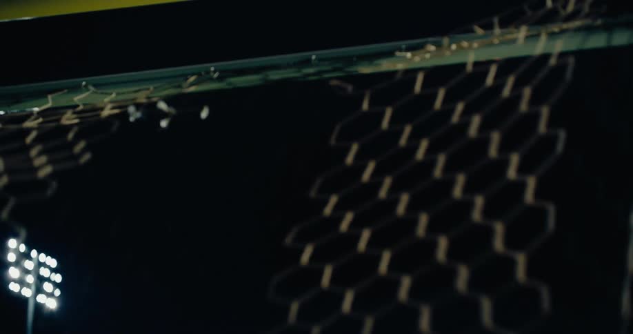 Man practices kicking a soccer ball into a soccer goal at night