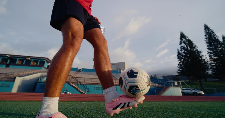 A man juggling soccer ball on the pitch in the evening