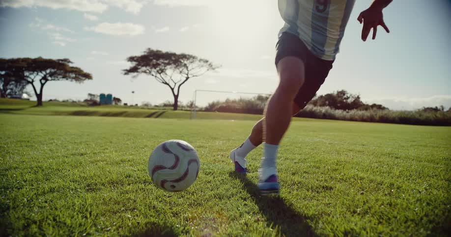 A soccer player wearing an argentina jersey dribbles a ball across a sunlit grass fieldafter performing a quick footwork maneuver the player kicks the ball forward and runs out of the frame