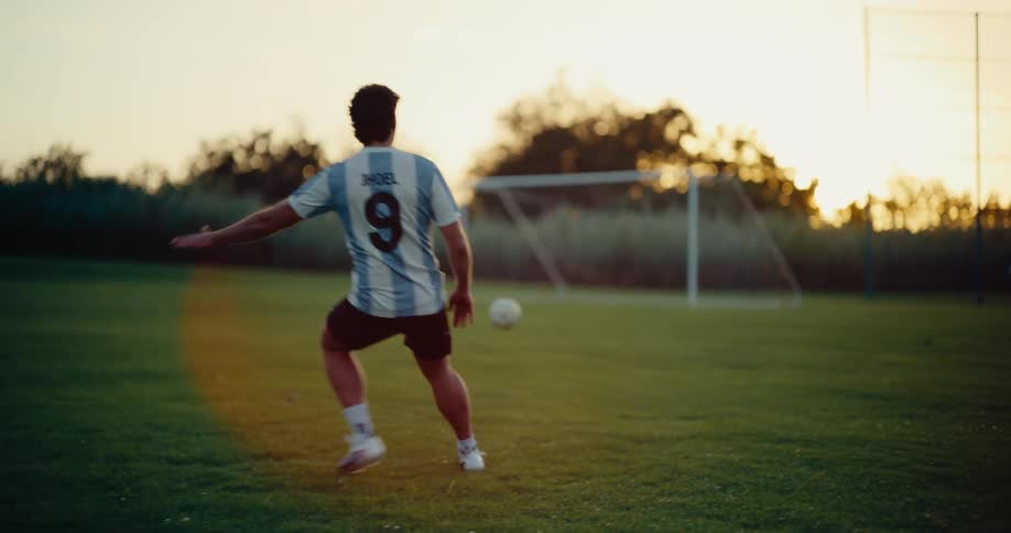 Man kicks a soccer ball at the goal on a field as the sun sits on the horizon