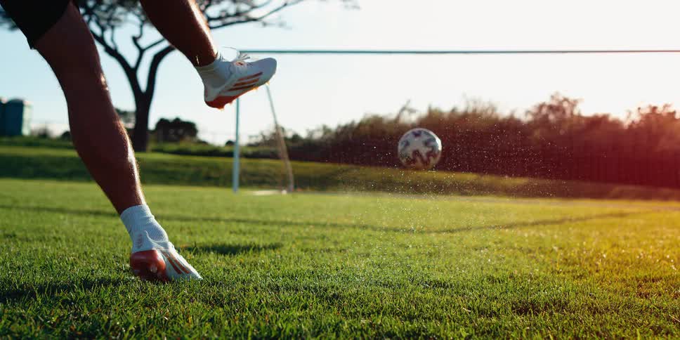 A soccer player kicks a ball into a soccer net at sunset