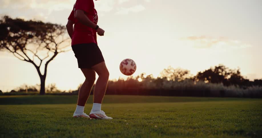 Soccer player standing in a field bouncing a soccer ball into the air with his feet