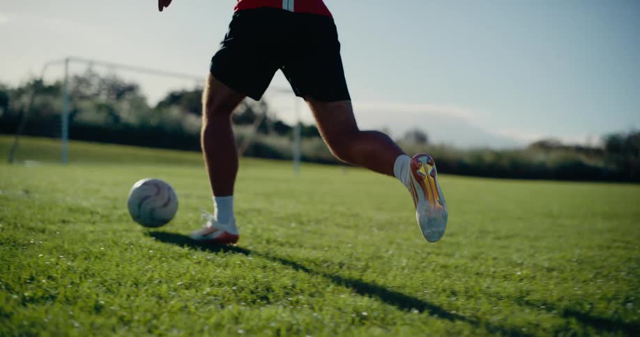 Male soccer player at the park dribbles the soccer ball and kicks it at the soccer goal on a summer day