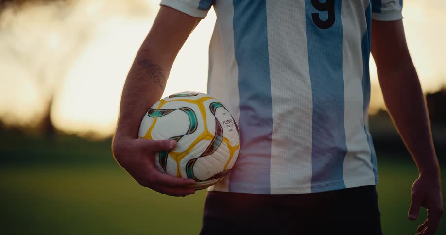 Player stands holding a soccer ball as the wind blows his jersey