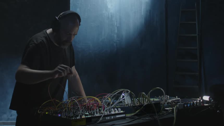 Man wearing headphones operating a sound mixer with cables and electronic modules
