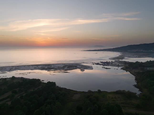 Sun sinks beneath the horizon as waves roll towards the shore under a cloudy sky