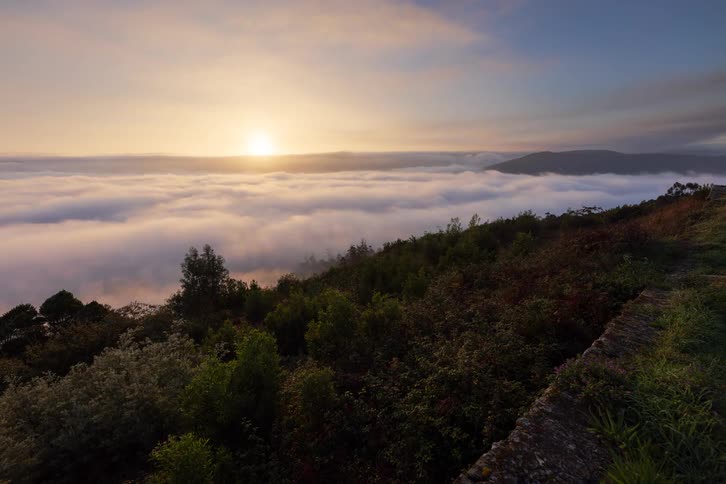 A time lapse shows clouds moving through a valley at sunrise from an elevated hillside perspective