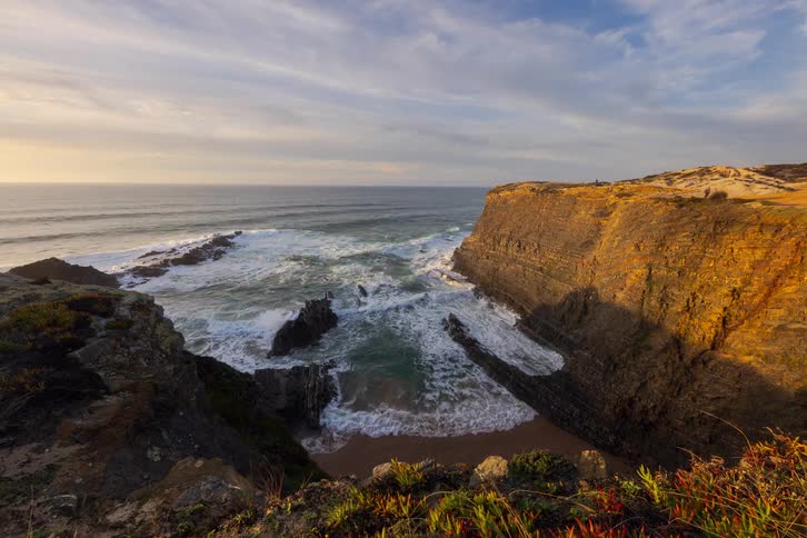 People walking on a cliff along the coast overlooking the water as waves roll into the shore