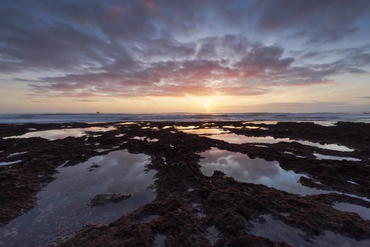 Time laps of the sun setting over the ocean near some tide pools